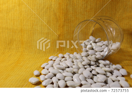 White dry beans in a jar lies spilled out on a yellow lemon background with a copy of the space White dry beans in a jar lies spilled out on a yellow lemon background with a copy of the space 72573755