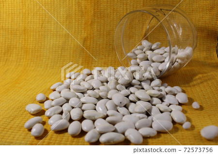 White dry beans in a jar lies spilled out on a yellow lemon background with a copy of the space 72573756