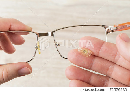 Hands hold eyeglasses and nose pad broke off them against brown desk. Hands hold eyeglasses and nose pad broke off them against brown desk. 72576383