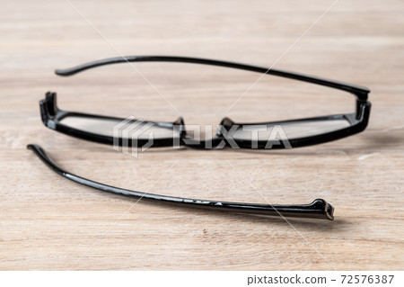 One eyeglasses temple in front of broken spectacles on a brown desk. One eyeglasses temple in front of broken spectacles on a brown desk. 72576387