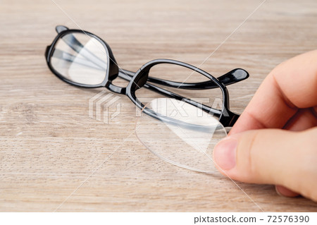 Fingers holds the fallen out lens in front of eyeglasses with the cracked rim. Fingers holds the fallen out lens in front of eyeglasses with the cracked rim. 72576390