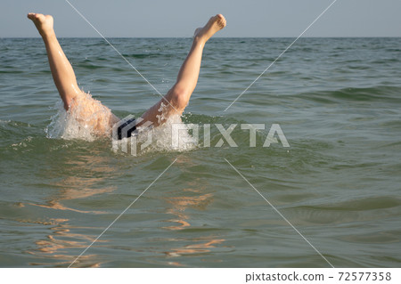 A 10-year-old boy is swimming, standing on his hands under water, feet on the surface. A 10-year-old boy is swimming, standing on his hands under water, feet on the surface. 72577358
