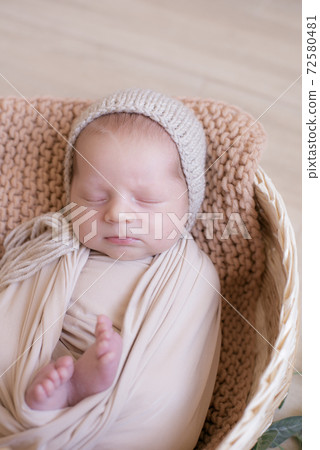 Cute little baby in a knitted hat with a toy bunny lies in a wicker basket decorated with greens and lemons in a beige knitted blanket. Summer mood. Happy healthy childhood 72580481