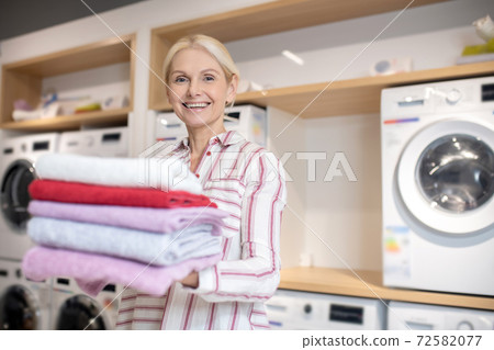 Smiling blonde woman holding a pile of towels and feeling good 72582077