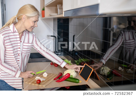 Woman standing in the kitchen and having a culinary video workshop 72582367