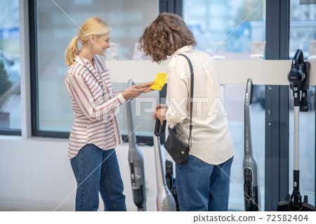 Female sales assistant in striped shirt showing new devices to the customer 72582404