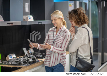 Sales assistant in striped shirt talking to female customer 72582423