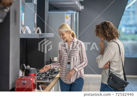 Sales assistant in striped shirt showing goods to the female customer 72582440