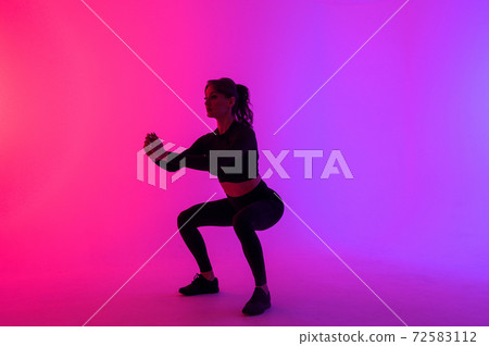 Full length portrait of a young fitness woman doing squatting isolated on a vibrant colors background 72583112