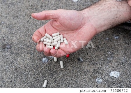 Male hand holding several pills. Access to prescription drugs and possible accidental overdose 72586722