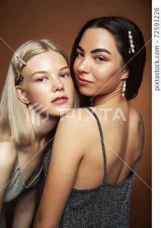 two pretty diverse girls happy posing together: blond and brunette on brown background, lifestyle people concept 72591226