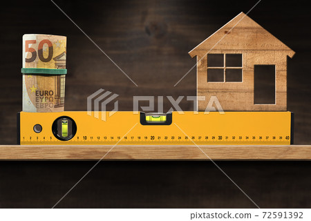 Construction Spirit Level with Roll of Euro Banknotes and a Model House 72591392