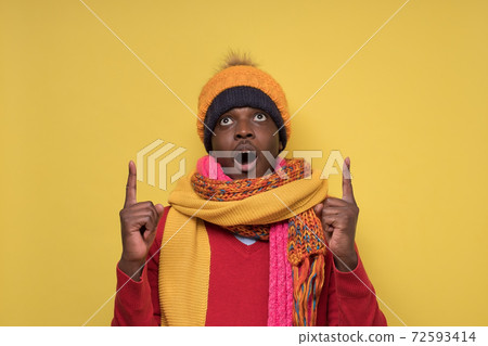 Man in several hat and scarfs opening mouth widely, pointing up at copy space 72593414