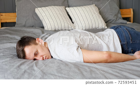Tired guy falls down on bed with grey linen and pillows Tired guy falls down on bed with grey linen and pillows 72593451