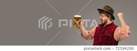 Happy smiling man dressed in traditional Austrian or Bavarian costume gesturing isolated on grey studio background 72594288