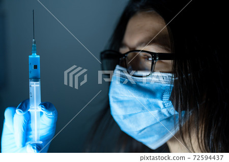 Young female doctor in a medical mask and gloves holds a syringe with a coronavirus vaccine and a vaccine chip inside. Conspiracy theory. Chipping people 72594437