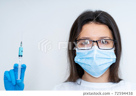 Young female doctor in a medical mask and gloves holds a syringe with a coronavirus vaccine and a vaccine chip inside. Conspiracy theory. Chipping people 72594438