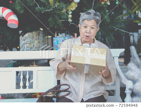 asian old elder woman elderly senior holding gift present box near christmas tree 72594948
