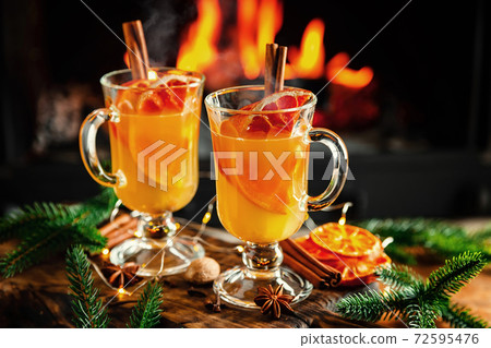 Mulled cider glasses on the background of fireplace fire. Hot mulled spiced apple cider cocktail for winter or autumn time. 72595476
