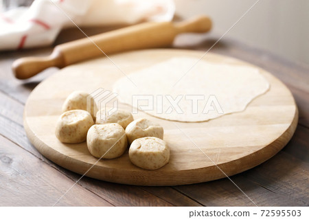 Rolled dough on a wooden board, a process of making homemade flatbreads 72595503