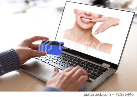 Payment for service via the internet. Female hands with credit card and open laptop with advertising of the dental industry in the screen, selective focus. Payment for service via the internet. Female hands with credit card and open laptop with advertising of the dental industry in the screen, selective focus. 72596446