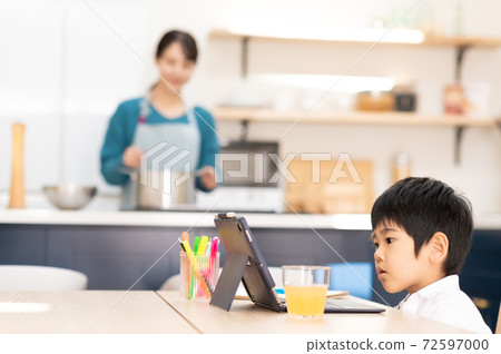 Mother cooking in the kitchen and boy taking online lessons at the table Mother cooking in the kitchen and boy taking online lessons at the table 72597000
