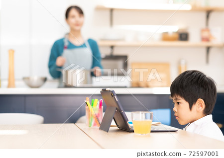 Mother cooking in the kitchen and boy taking online lessons at the table Mother cooking in the kitchen and boy taking online lessons at the table 72597001