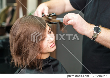Hairdresser straightening brown hair with hair irons. 72598043