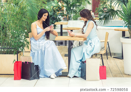 Two casual young women looks to smartphone after shopping at outdoors cafe. Two casual young women looks to smartphone after shopping at outdoors cafe. 72598058