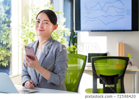 Business woman operating a smartphone in a bright office 72598420
