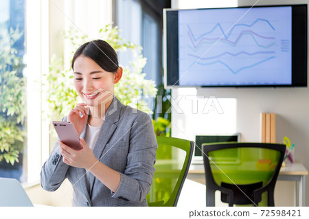 Business woman operating a smartphone in a bright office 72598421