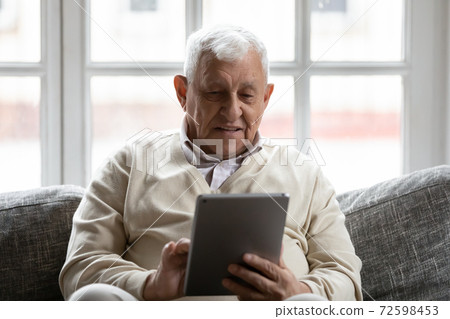 Positive retired man relaxing on comfy couch using tablet computer 72598453