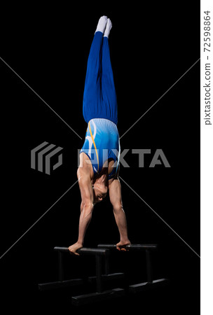 Muscular male gymnast training in gym, flexible and active. Caucasian fit guy, athlete in blue sportswear isolated on black Muscular male gymnast training in gym, flexible and active. Caucasian fit guy, athlete in blue sportswear isolated on black 72598864