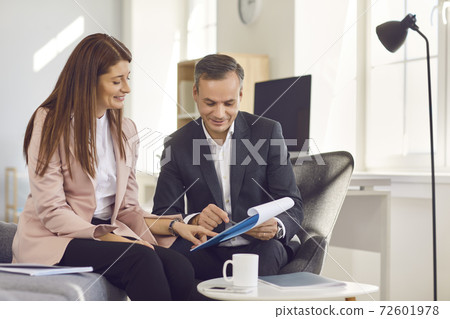 Adult male manager showing his assistant a notebook with new ideas while sitting in the office. 72601978