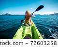 Woman paddling a kayak at sea with distant mountains ahead 72603258