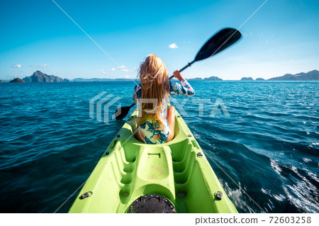 Woman paddling a kayak at sea with distant mountains ahead 72603258