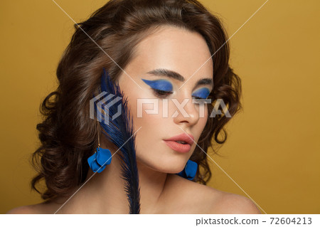 Beautiful young woman with brown curly hair and makeup on yellow background 72604213