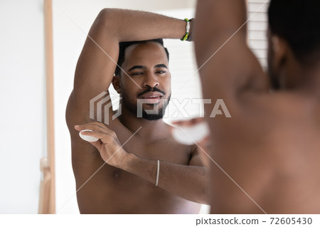 Happy millennial african american man applying dry deodorant stick. Happy millennial african american man applying dry deodorant stick. 72605430