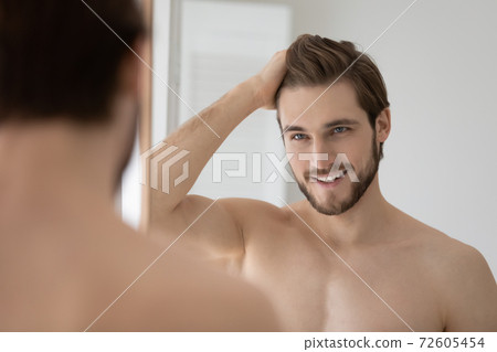 Happy shirtless confident young man styling hair with fingers. 72605454
