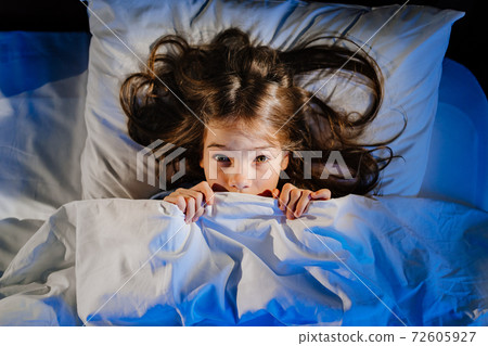 frightened girl covers his face with a blanket in bed in her room. child's fear 72605927