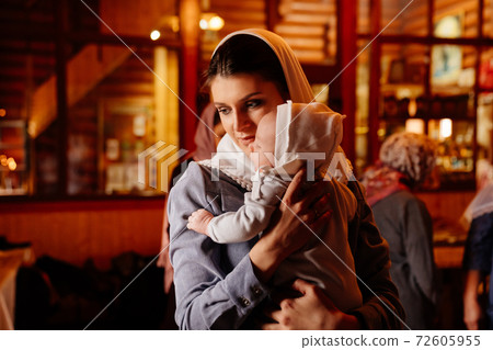 beautiful mom in a headscarf with a small child in her arms in church. beautiful mom in a headscarf with a small child in her arms in church. 72605955