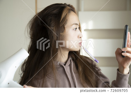 A woman drying her hair with a hair dryer 72609705