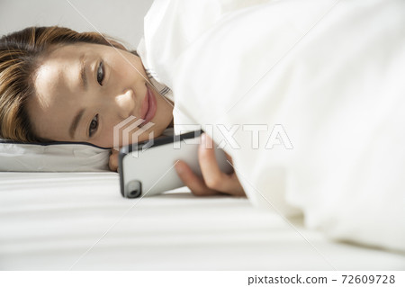 A woman looking at a smartphone while waking up A woman looking at a smartphone while waking up 72609728