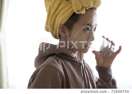 A woman drinking water after taking a bath 72609754