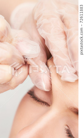 Forehead injection at spa salon. Doctor hands. Pretty female patient. 72611883