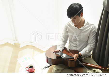 Portrait of young man sitting on floor with tablet for search lyrics in modern home. 72613754