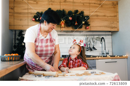 Grandma and granddaughter look at each other while making cookies in the kitchen. 72613809