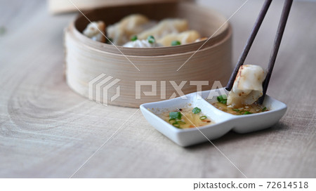 Close up shot of chopsticks holding dumpling dipping into plum sauce on wood table. Close up shot of chopsticks holding dumpling dipping into plum sauce on wood table. 72614518