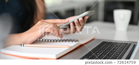 Cropped shot of young woman freelancer using mobile phone while sitting at her workplace. Cropped shot of young woman freelancer using mobile phone while sitting at her workplace. 72614759