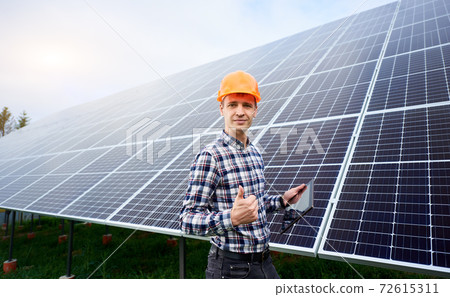 Electrician in a helmet with a tablet in his hands shows thumb up like against solar panels 72615311